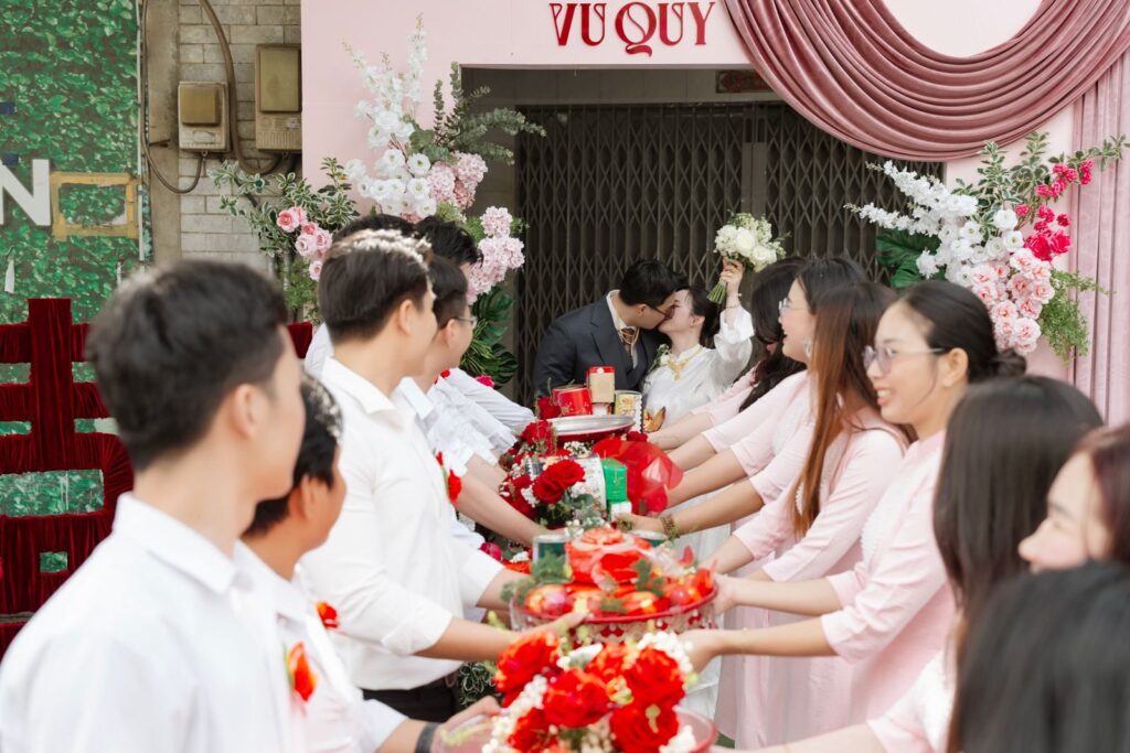 Bride and groom kiss surrounded by family in a vibrant Vietnamese wedding celebration.